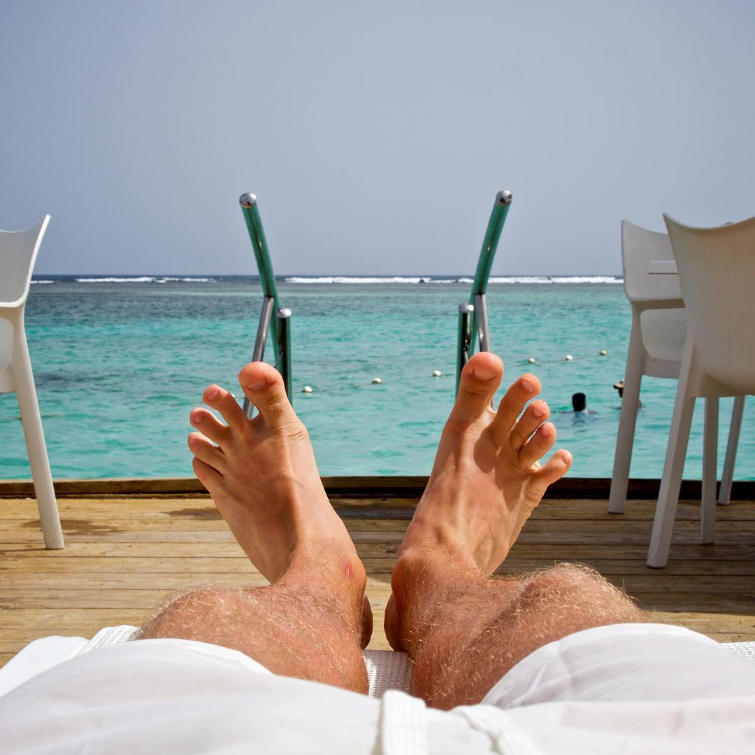 Расслабьтесь и наслаждайтесь. Мужские ноги на пляже. Отпуск. Мужские ноги. Парень отдыхает.
